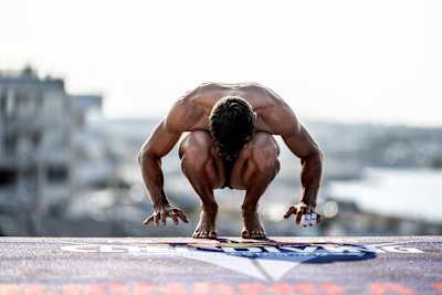 Romania's Constantin Popovici crouches on the 27.5 metre platform in Polignano a Mare, Italy, during Red Bull Cliff Diving World Series training, showcasing elite athletic focus in 2023