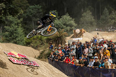 Red Bull Hardline Tasmania 2025 sees George Brannigan soaring on his bike over a jump at Maydena Bike Park, captivating a crowd of spectators during the thrilling mountain bike race
