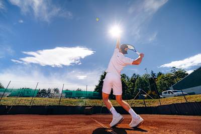 Nicolai Budkov Kjær, wearing a Red Bull cap, unleashes a forehand on a clay tennis court in Norway under the summer sun in July 2026