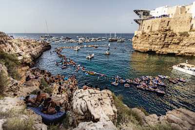 Spectators crowd the cliffs and rafts as Meili Carpenter dives from the 27.5 metre platform at the 2024 Red Bull Cliff Diving World Series in Polignano a Mare, Italy