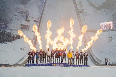 Winning teams stand atop the Red Bull Target Jumping 2026 podium amid blazing fire effects in snowy Zakopane, Poland, capturing the thrill and energy of this legendary winter event.