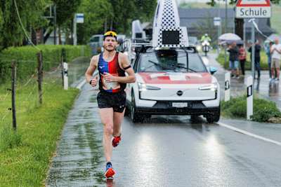 Slovenian athlete Domen Hafner powers down a rainy street in Zug, Switzerland during the 2025 Wings for Life World Run with the Red Bull-branded Catcher Car close behind.