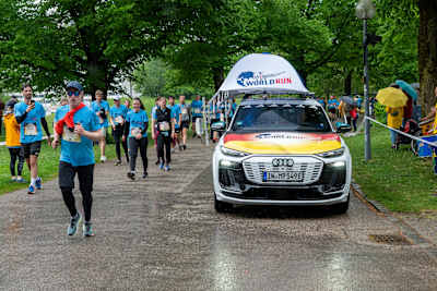 Teilnehmer:innen nehmen die Herausforderung beim Wings for Life World Run 2025 in München an, während das offizielle Catcher Car sie im Regen überholt.