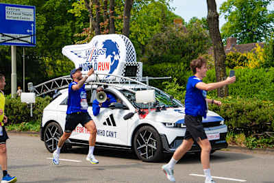 In Breda, 2026, Kjeld Nuis and Churandy Martina energise the Wings for Life World Run, racing alongside the Red Bull branded catcher car in a vibrant street marathon