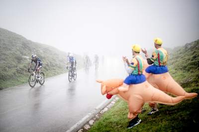 Red Bull - BORA - hansgrohe rider Daniel Felipe Martínez climbs through mist on the Covadonga finish of La Vuelta 2024, cheered by fans in inflatable kangaroo costumes.