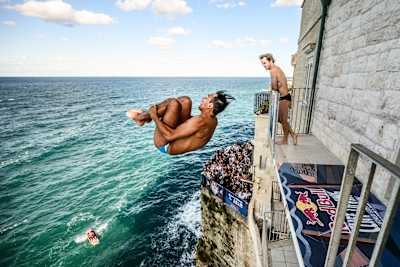 Sergio Guzman of Mexico launches from the 26-metre balcony as Gary Hunt watches during the 2026 Red Bull Cliff Diving World Series in Polignano a Mare, Italy