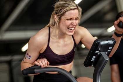 Eine entschlossene Teilnehmerin trainiert auf einem Fitnessrad beim Red Bull Pit Race während des Red Bull HYROX-Trainingslagers auf dem Silverstone Circuit in Großbritannien.