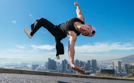 In 2024, B-Boy Phil Wizard performs an acrobatic freeze mid-air against Cape Town's skyline backdrop