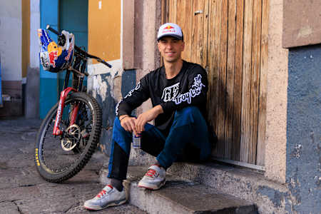 Pedro Burns sitting on doorway steps, his bike behind him with Red Bull helmet hanging on handlebars