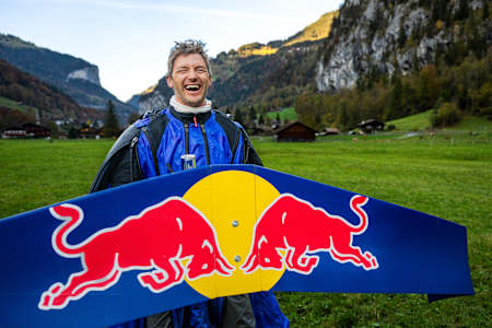 In 2024, Peter Salzmann joyfully holds a Red Bull wingsuit in the Swiss Alps near Lauterbrunnen.