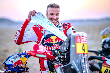 En 2024, Sam Sunderland de Red Bull GAS Factory Racing, rayonnant de joie, brandit son roadbook de rallye sur la ligne de départ de l'étape du rallye Dakar en Arabie saoudite.