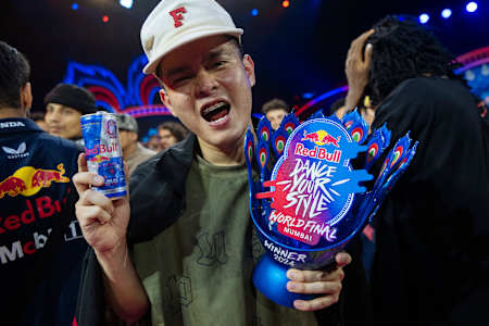 In 2024, MT Pop celebrates at the Red Bull Dance Your Style World Final event in Mumbai, India, holding a Red Bull can and winner's trophy