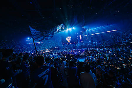 In 2024, a massive crowd at the Red Bull League of Its Own event at the Accor Arena in Paris, France, with a checkered flag waving amidst bright blue lights.