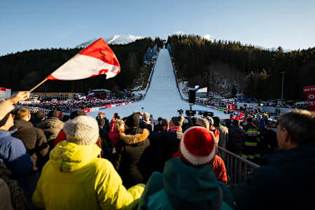 A dynamic crowd of Red Bull fans bring excitement to the 2024 ski flying championships at Kulm in Bad Mitterndorf, Austria, cheering under crisp alpine skies as athletes soar down the slope