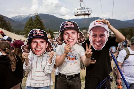 In 2024, smiling fans hold up athlete cutouts at the Red Bull Joyride event in Whistler, Canada, with mountains and a chairlift in the background