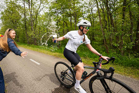 A dynamic participant grabs a refreshment while cycling through lush forests during Red Bull 211 in Nida, Lithuania on May 24, 2025.