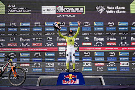 Jackson Goldstone celebrates his victory at the UCI Mountain Bike World Cup 2025 in La Thuile, Italy, raising his helmet on the podium.