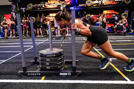 Athletes power through intense fitness challenges, pushing 100kg, at the Red Bull HYROX Coaches Camp, at the iconic Silverstone Circuit in the UK, with Red Bull Racing cars on display in 2025.