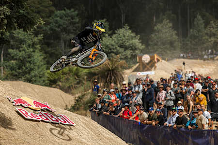 Red Bull Hardline Tasmania 2025 sees George Brannigan soaring on his bike over a jump at Maydena Bike Park, captivating a crowd of spectators during the thrilling mountain bike race