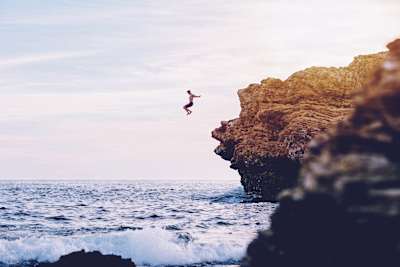An adventurer jumps off cliff into the sea.