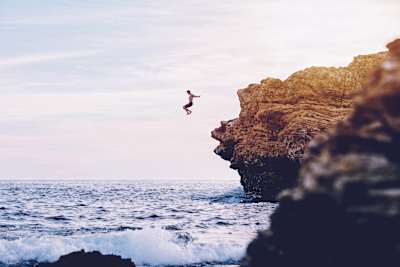 An adventurer jumps off cliff into the sea.