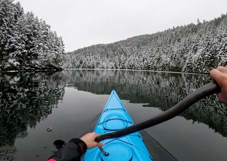 Benny Marr paddles through black water in wintertime with trees and snow.