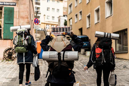 Trzy osoby z dużymi plecakami idące ulicą w mieście.