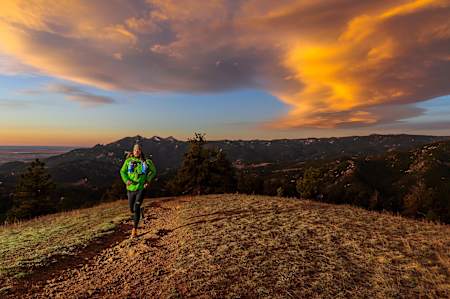 Runner comes over hill with sunset behind them.