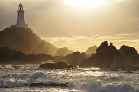 The evening sun is shining on the Corbiere Lighthouse in Jersey.