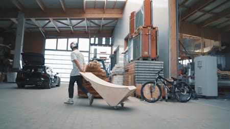 MTB-Ass Erik Fedko rollt seine neue MTB-Rampe auf den daran angebrachten Rollen an seinem MTB vorbei zu seinem Audi.