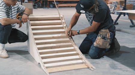 MTB-Ass Erik Fedko und IOU Ramps Inhaber Andreas Schützenberger markieren die Schraublöcher auf einer Holzleiste, bevor sie den Belag auflegen.