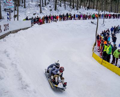 Teilnehmer:innen fahren bei Red Bull Bob Heroes die Bobbahn hinunter und werden dabei vom Publikum angefeuert, die zahlreich zu diesem spektakulären Event gekommen sind.