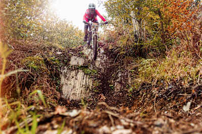 Rider approaches steep rock drop in an autumnal setting.