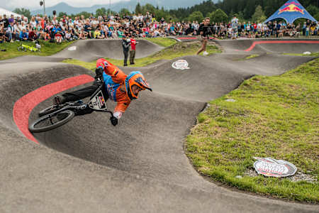 Rider on BMX comes around berm during pump track race.