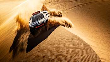 A rally car send sand flying in the dunes during the Dakar Rally.