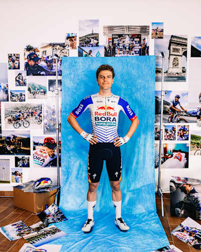 Arne Marit stands proudly in Red Bull - BORA - hansgrohe kit for a dynamic 2025 season portrait, captured in Fuschl, Austria, with vibrant cycling images in the background