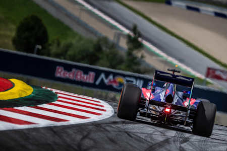 A photo of Marc Márquez racing a Toro Rosso F1 car around the Spielberg circuit in Austria.