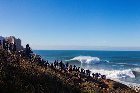 Spectators on the cliffside watch the surfers in the waves below at Nazaré.
