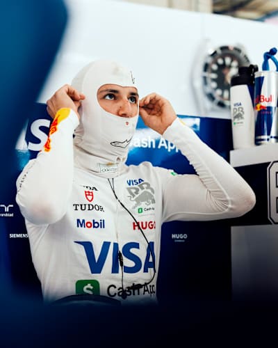 Isack Hadjar adjusts the hood of his Visa Cash App Racing Bulls race overalls before a Grand Prix drive. 
