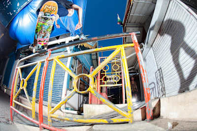 TJ Rogers locks a tall frontside crooked grind on a short round rail slap bang in the middle of a closed Mauritian market gangway.