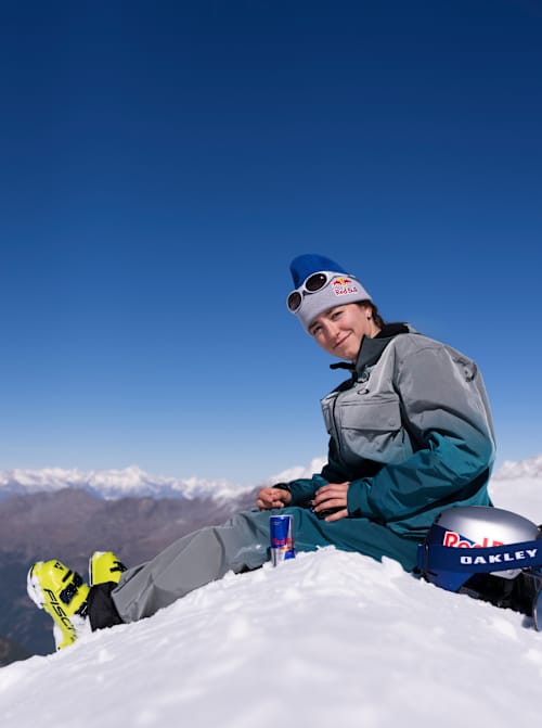Beim Red Bull Performance Camp 2025 in Saas-Fee, Schweiz, entspannt sich Mathilde Gremaud auf verschneiten Pisten mit Red Bull und Oakley-Ausrüstung unter blauem Himmel.