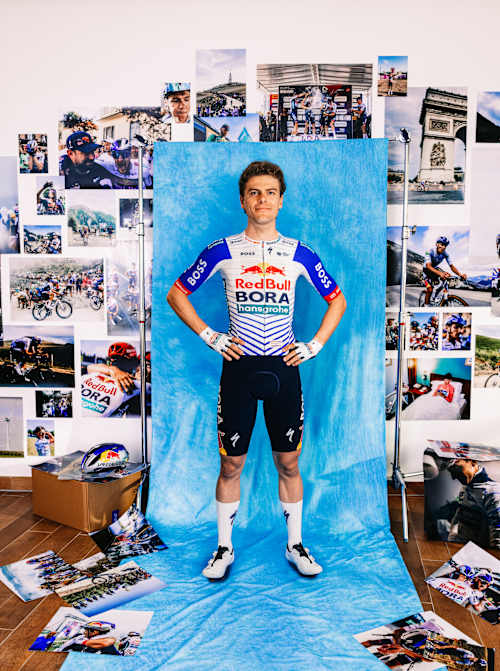 Arne Marit steht stolz im Red Bull - BORA - hansgrohe Trikot für ein Porträt der Saison 2025 in Fuschl, Österreich, mit eindrucksvollen Radsportbildern im Hintergrund.