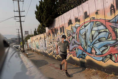 Rickey Gates runs past graffiti wall with mask on during his 46 day marathon to run every single street in the city of San Francisco, California, USA.