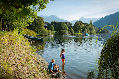 People sit and stand in the lake waters at Zell am See.