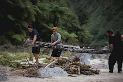 Rob Warner, Josh James and Matt Jones carry a tree trunk to their wilderness camp in the Buller District of New Zealand.