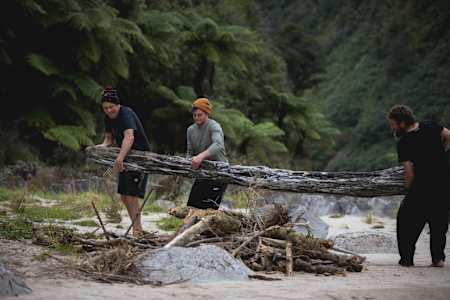 Rob Warner, Josh James and Matt Jones carry a tree trunk to their wilderness camp in the Buller District of New Zealand.