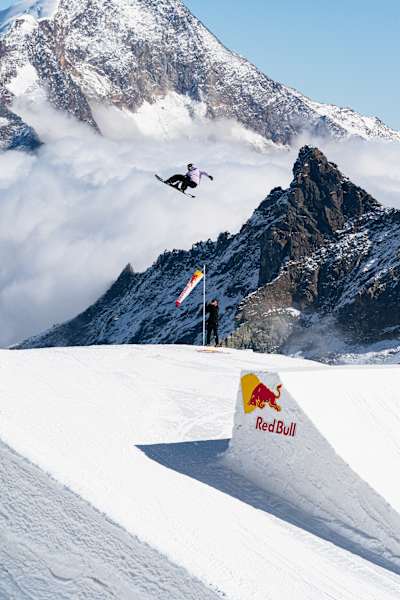 Yiming Su mid air executing a stylish Crail rotation above the Red Bull Performance camp jump in Saas-Fee, Switzerland, on October 1st, 2025, surrounded by stunning alpine peaks.