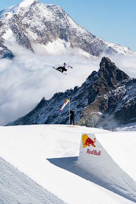 Yiming Su in der Luft bei einer stylischen Crail-Rotation beim Red Bull Performance Camp in Saas-Fee, Schweiz, am 1. Oktober 2025, umgeben von atemberaubenden Berggipfeln.