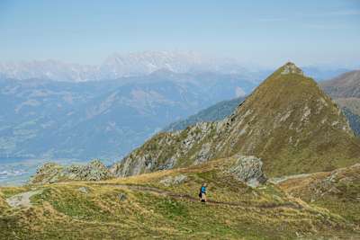 Person runs along a mountain track in Austria with far reaching mountain views in the distance.