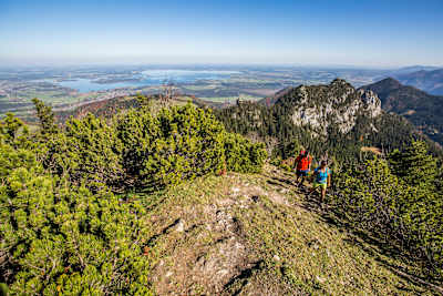 Zwei Wanderer sind in den Chiemgauer Alpen unterwegs, im Hintergrund schimmert der Chiemsee.